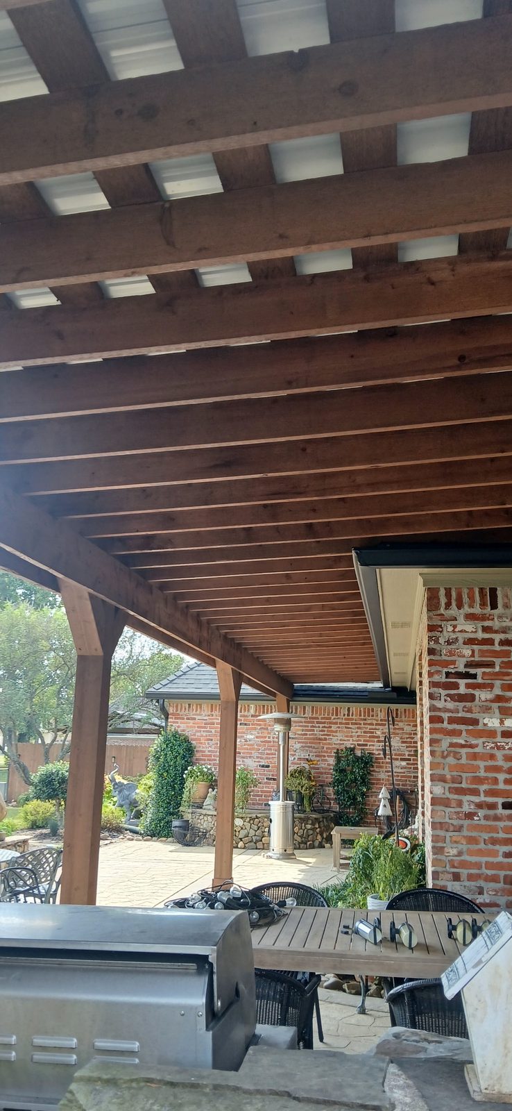 Outdoor covered patio with cedar beam ceiling and brick fireplace in Bossier City